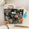 A dark floral patterned cosmetic pouch with pink and green accents rests on a light surface next to a makeup brush.