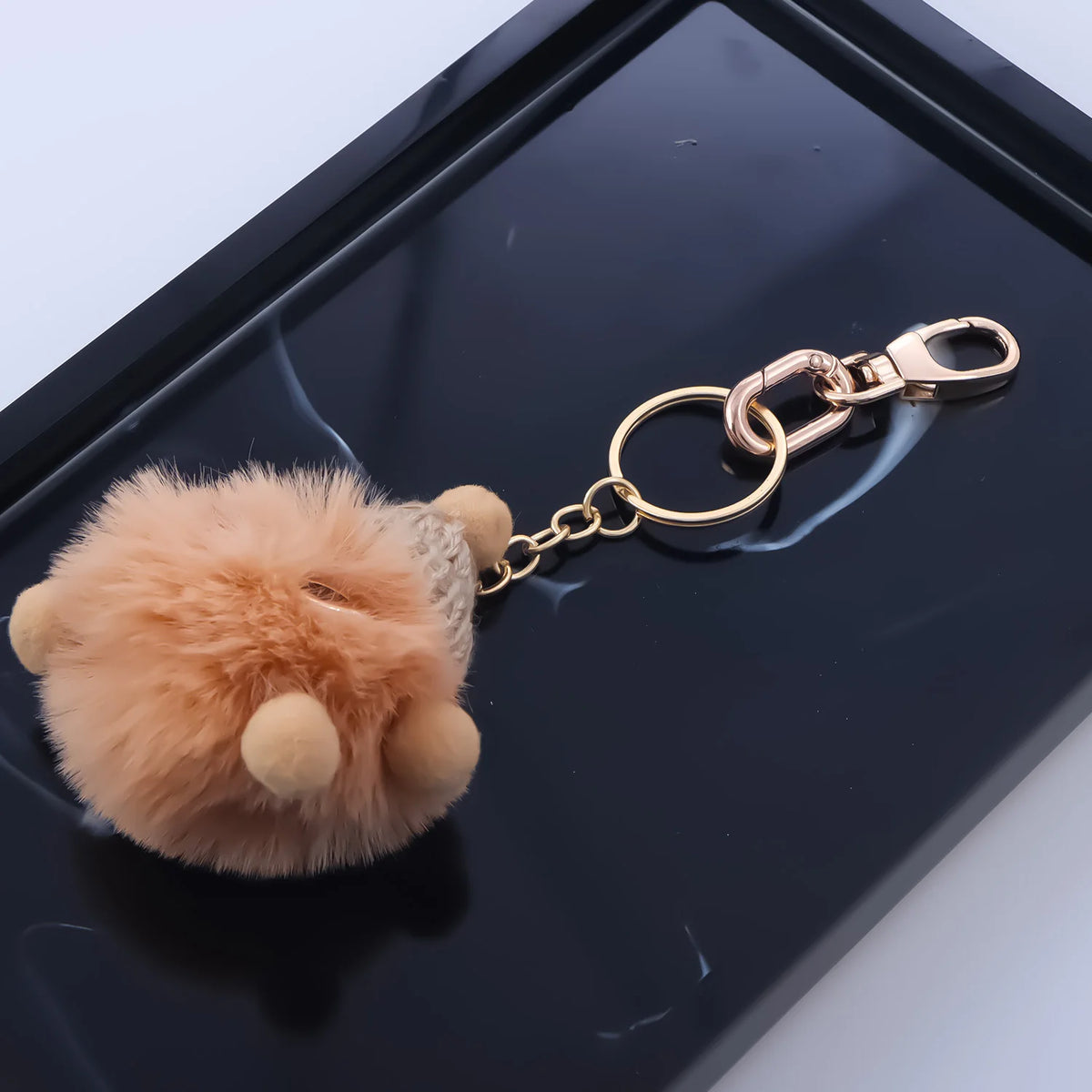 A small, fluffy, light orange-brown animal figurine attached to a gold metal swivel lobster claw clasp.
