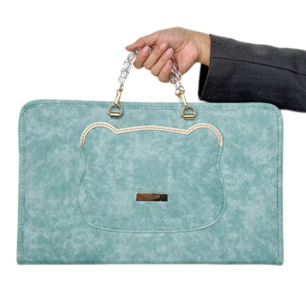 A hand holds a light blue suede laptop protective case with a leather trim and silver chain strap.