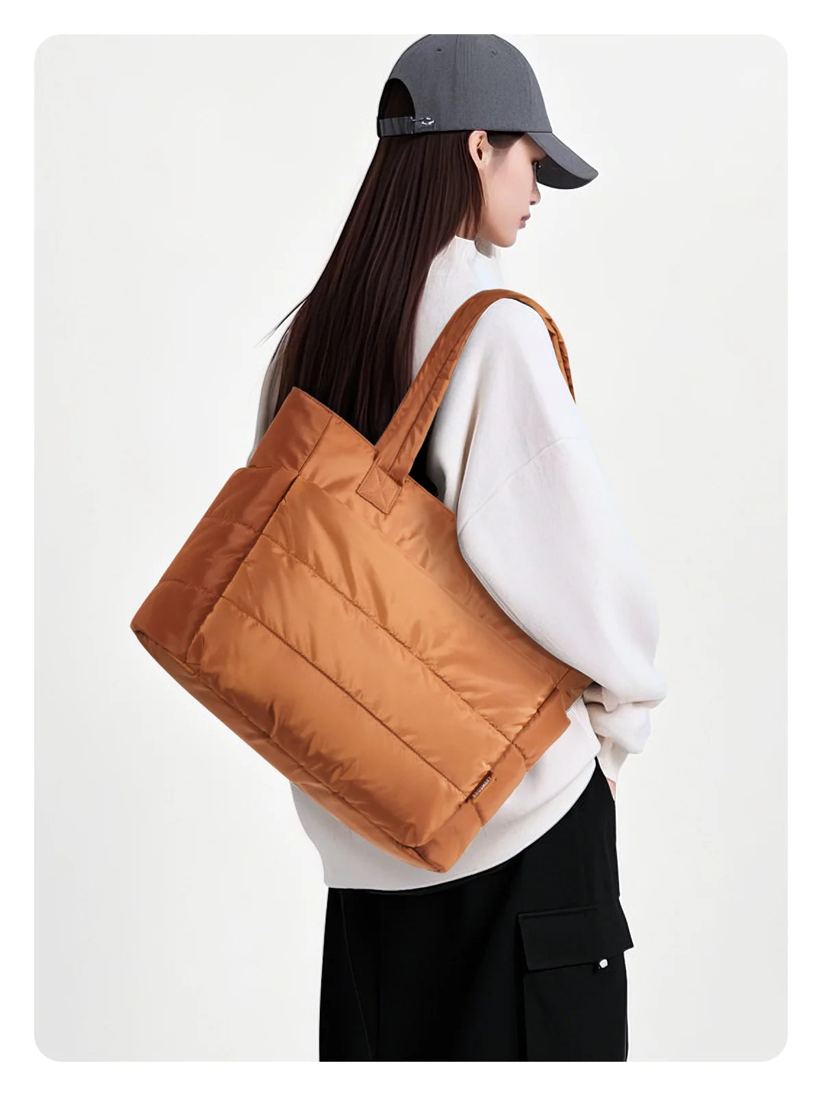 Une femme portant une casquette grise et un pull blanc tient un sac à main rembourré marron et matelassé.