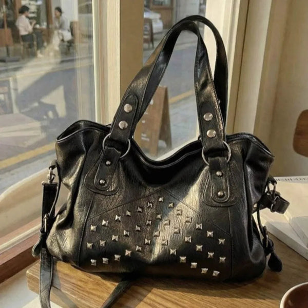 Schwarze Punk-Rivet-Leder-Tasche auf Holzoberfläche neben einem Fenster