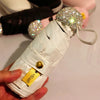 A white compact umbrella with a rhinestone sphere and gold accents is held in a hand.