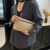Una mujer sostiene un elegante bolso de mimbre color beige claro contra un blazer gris oscuro.