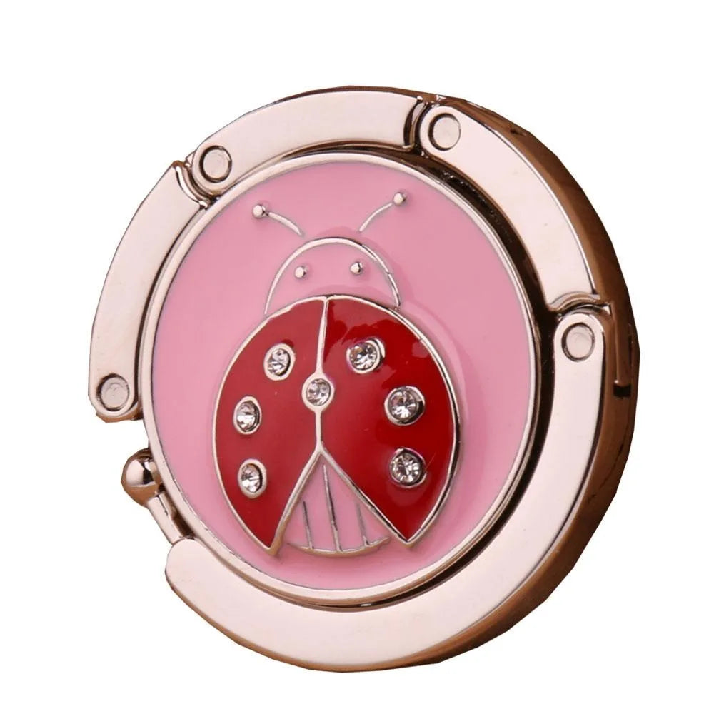 Ganchillo de mesa plegable de aluminio con forma de mariposa rosa y oro rosa.