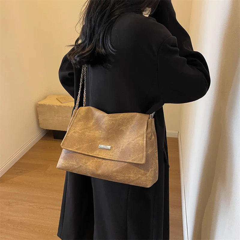 Una mujer con un abrigo negro sostiene un bolso de cuero marrón con una cadena dorada.
