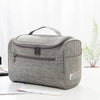 A gray portable Oxford cloth toiletry bag lying on a white surface with a pencil nearby.