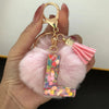 A hand holds a custom initial letter keychain featuring a shiny resin pendant and a pink alphabet charm.