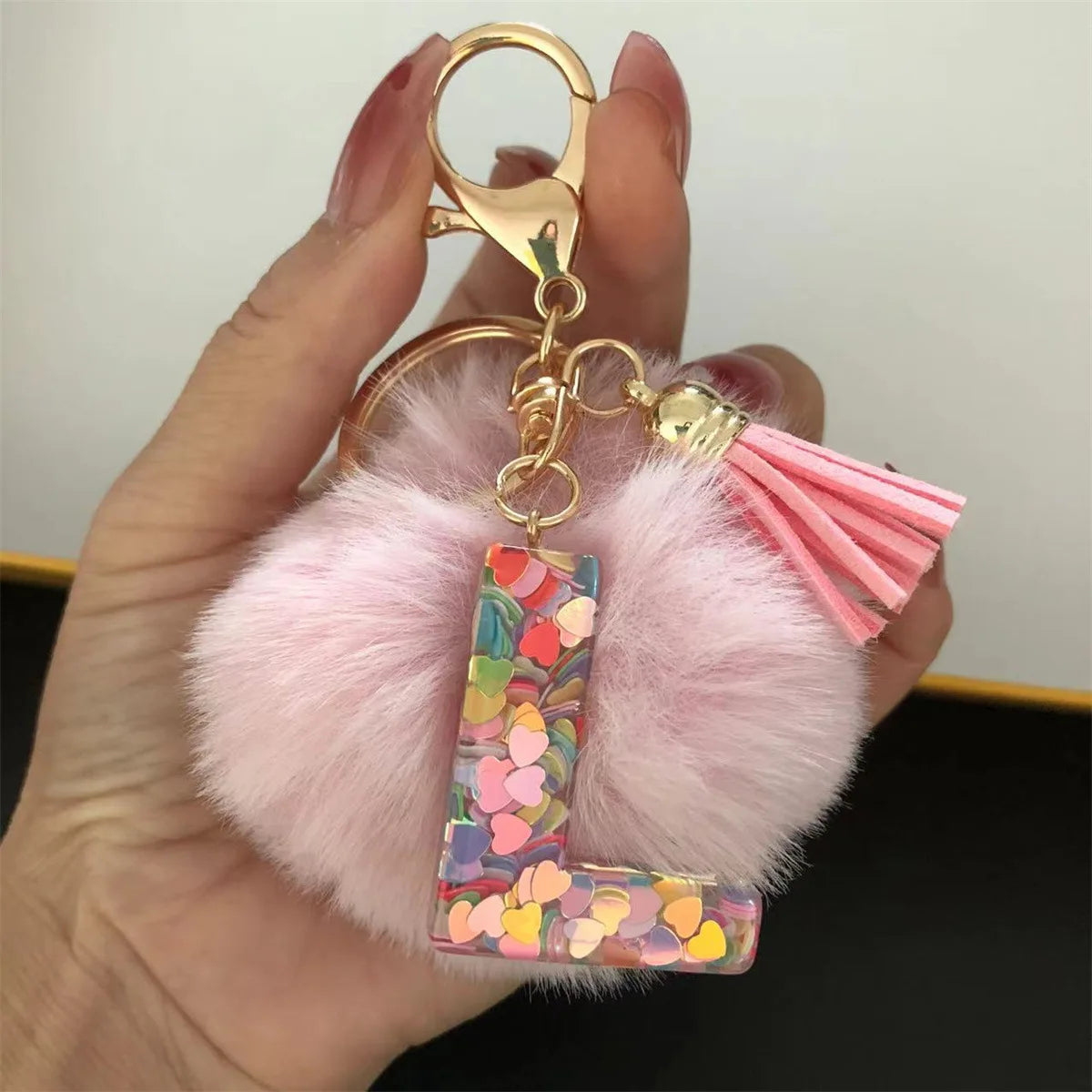 A hand holds a custom initial letter keychain featuring a shiny resin pendant and a pink alphabet charm.