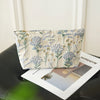 A light beige floral canvas makeup bag featuring blue and green botanical patterns, resting on a dark surface.