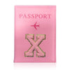 A pink leather passport holder with a gold embossed letter X and a pink airplane symbol.