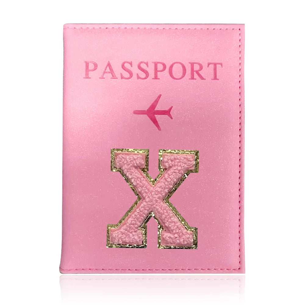 A pink leather passport holder with a gold embossed letter X and a pink airplane symbol.