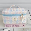 A light pink and blue quilted cosmetic bag with a zipper and a small tag resting on a pink book.