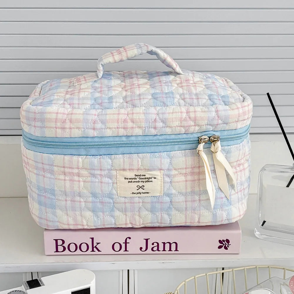 A light pink and blue quilted cosmetic bag with a zipper and a small tag resting on a pink book.