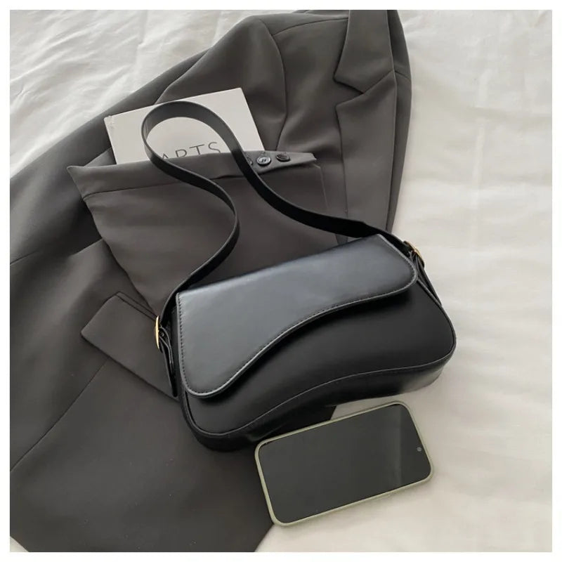 A dark gray blazer with a black leather flap shoulder bag and a smartphone resting on a white surface.