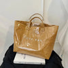 Una bolsa tote minimalista de PVC marrón claro exhibida contra un fondo blanco.