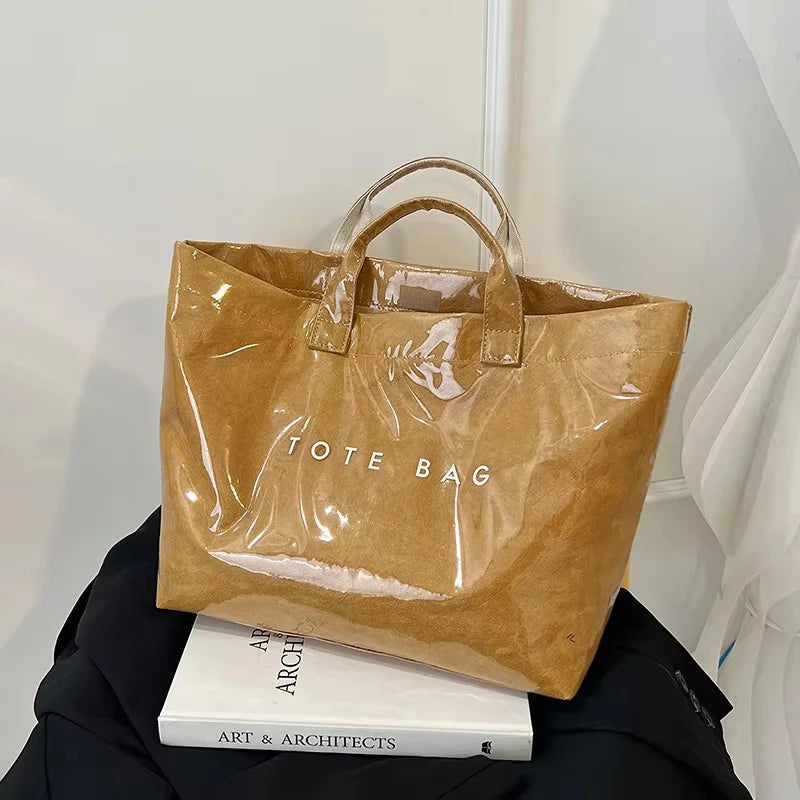 Una bolsa tote minimalista de PVC marrón claro exhibida contra un fondo blanco.