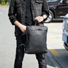 A person is holding a black full-grain leather backpack in an outdoor setting.