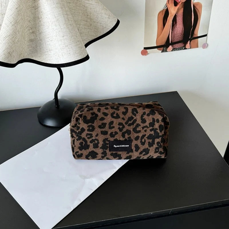 A brown leopard print makeup organizer bag resting on a black surface next to a white sheet of paper.