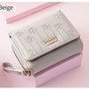 A beige compact PU leather women's wallet with a zipper closure and floral embroidery is shown resting on a pink surface.