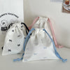 Three canvas makeup bags in white, pink, and blue with bowknot ties are displayed on a white surface.