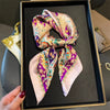 A silk paisley scarf tied in a bow is displayed in a black frame.