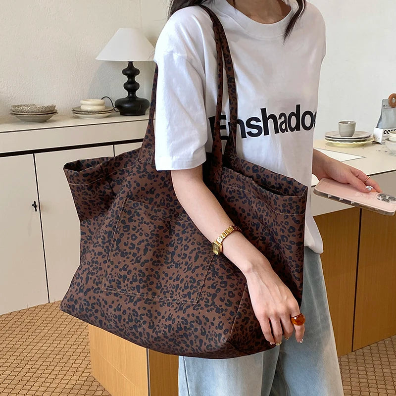 A person holds a brown leopard print canvas tote bag in front of a white shirt.
