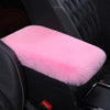 A pink plush cushion is placed on a black car armrest.