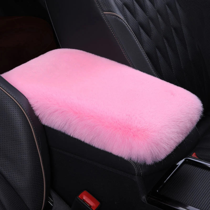 A pink plush cushion is placed on a black car armrest.
