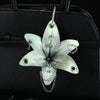 A realistic white orchid flower keychain is displayed against a black leather handbag.