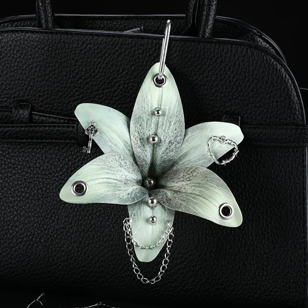 A realistic white orchid flower keychain is displayed against a black leather handbag.