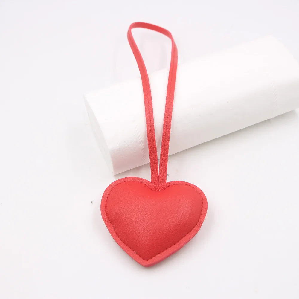 A red PU leather heart shaped keychain attached to a white rolled object.