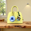 A yellow PU leather handbag with a handle and a blue floral charm resting on a wooden table.