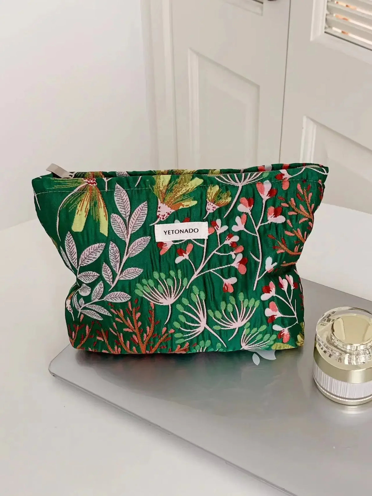 A vibrant green cosmetic pouch with floral embroidery and a white tag labeled YETONADO resting on a gray surface.
