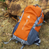 An orange and gray LBD Sports Club hiking backpack resting on dry grass next to a large rock.