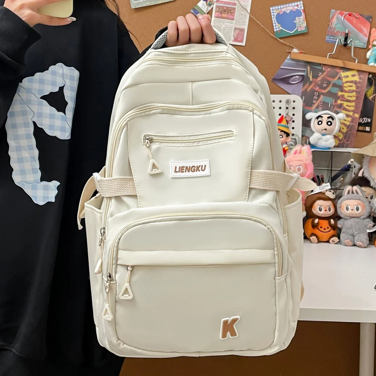A cream-colored lightweight nylon college backpack being held by a person against a brown background.