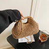 Une main tient un sac à main en paille tissée sur l'épaule contre un fond clair.