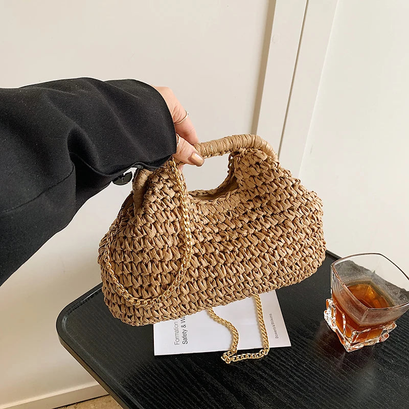 Une main tient un sac à main en paille tissée sur l'épaule contre un fond clair.