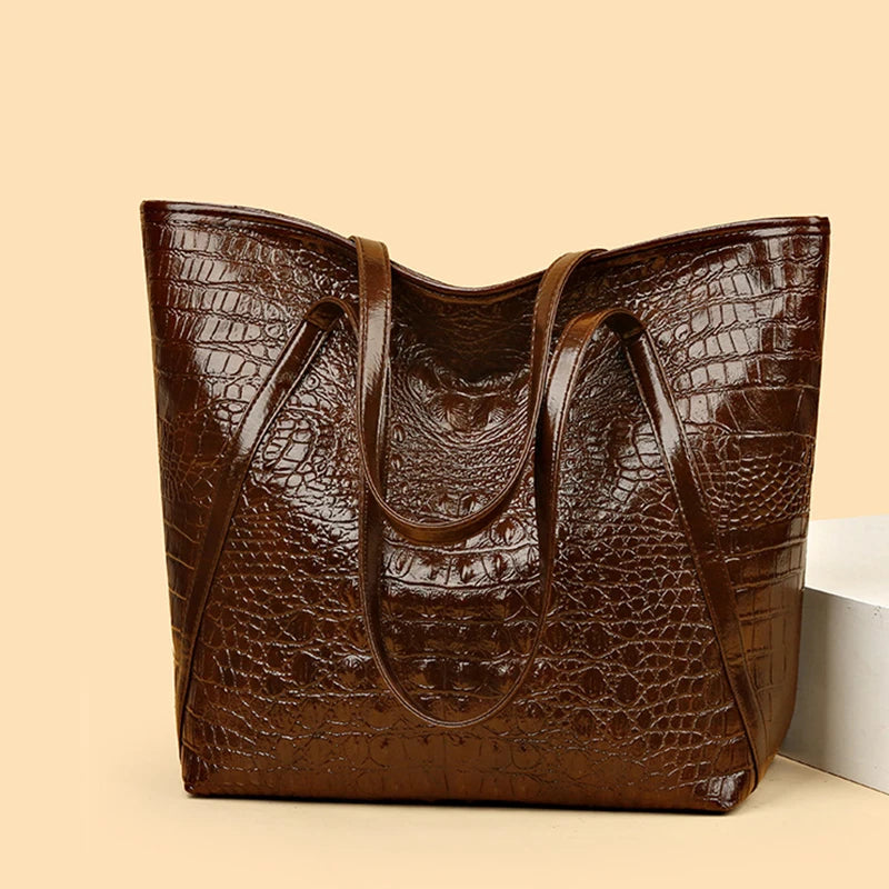 A brown crocodile print tote bag is shown in a studio setting.