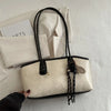 A beige PU leather tote bag with black handles and gold hardware resting on a white textured surface.