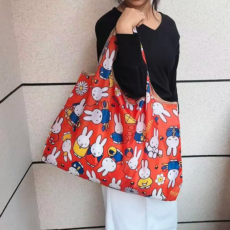 A person holds an orange and white Miffy folding shopping bag against a light background.