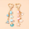 Gold heart-shaped keychain featuring a starfish and pearl accents with striped beads.