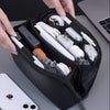 A hand is holding a black leather multi-layer cable organizer pouch filled with various white and black electronic cables.