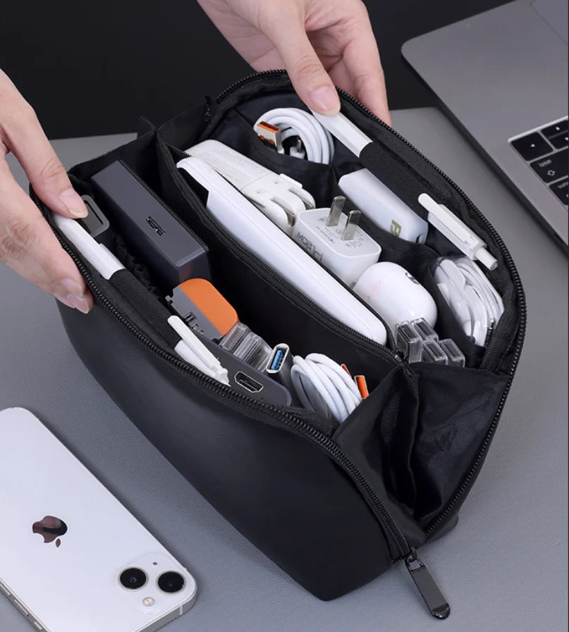 A hand is holding a black leather multi-layer cable organizer pouch filled with various white and black electronic cables.