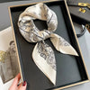 A beige paisley silk hair scarf tied in a bow is displayed in a black tray.