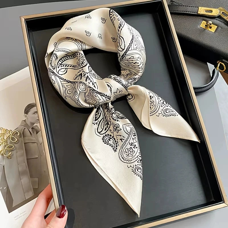 A beige paisley silk hair scarf tied in a bow is displayed in a black tray.