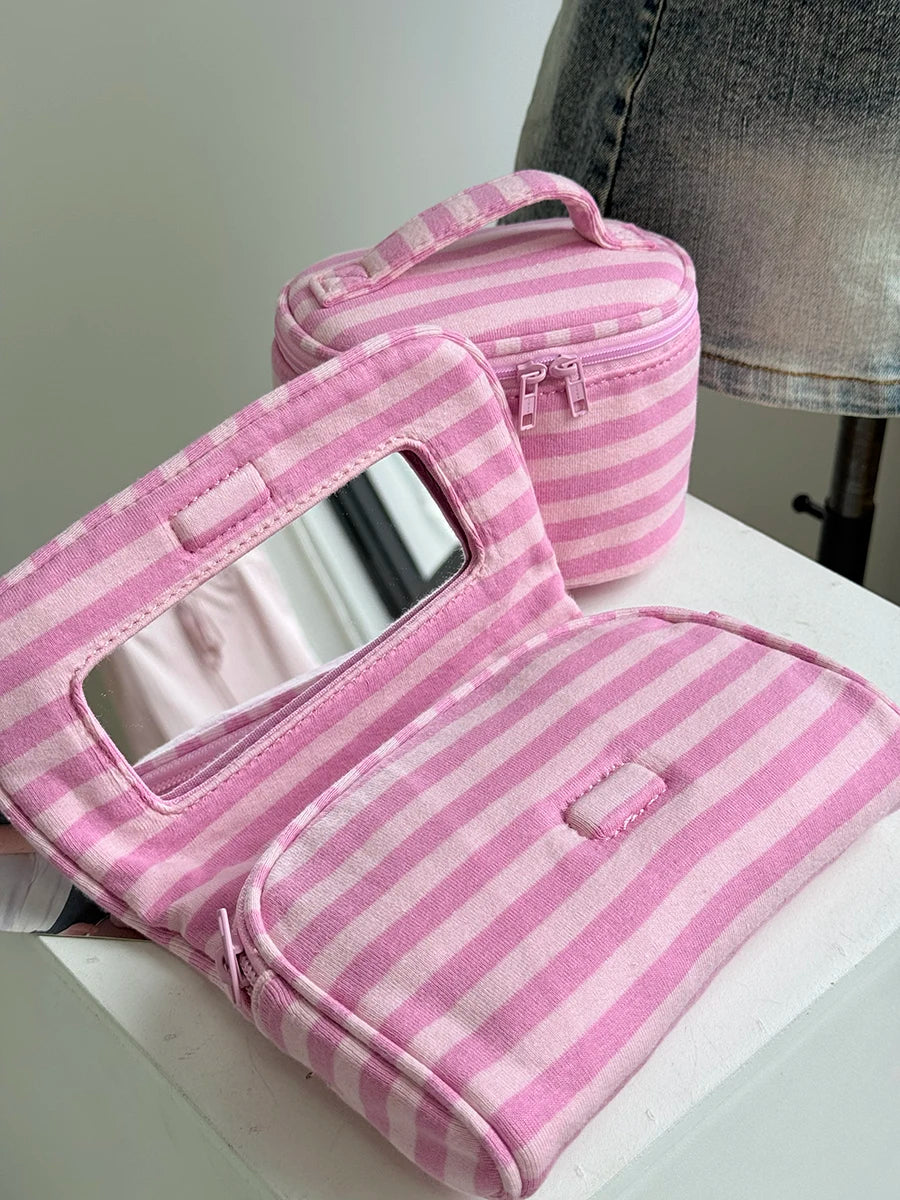A pink and white striped Y2K makeup bag with a clear mirror and zipper is displayed on a white surface.