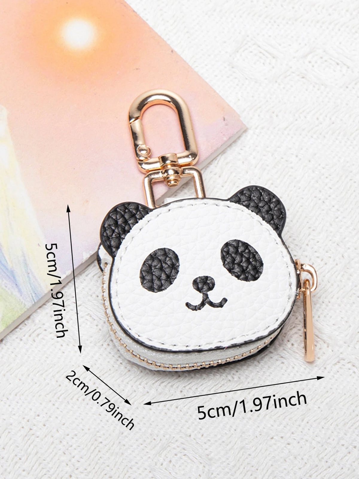 Cartera de moneda de panda blanco y negro con llavero dorado sobre fondo claro.