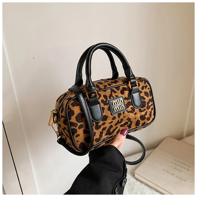 Braun-schwarze Leopardenmuster-Designer-Hobo-Tasche mit schwarzem Lederbesatz, gehalten von einer Hand.