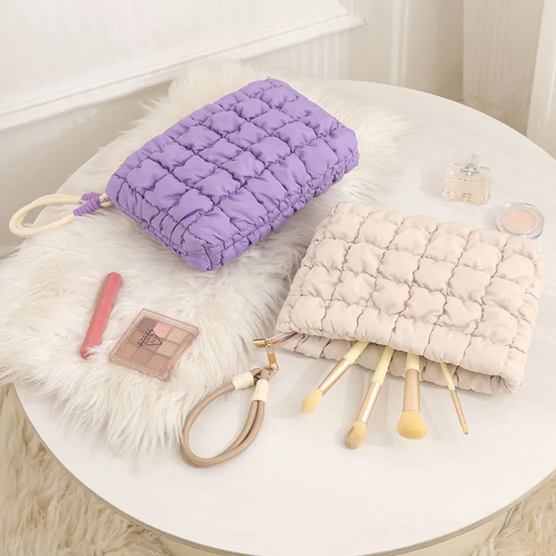 A purple quilted puffer makeup bag rests on a white fluffy rug next to cosmetic brushes.