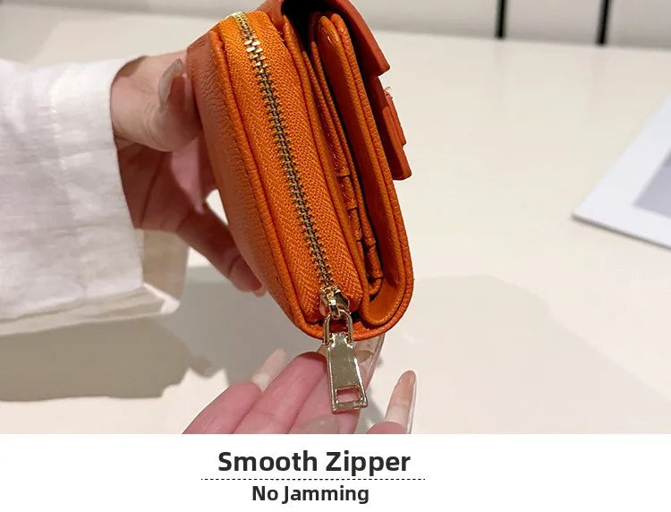 An orange zippered card holder with a gold zipper pull is being held by a hand.